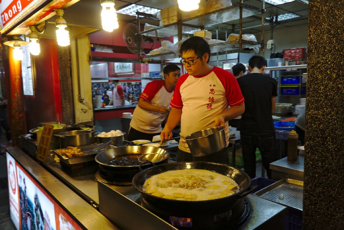 Street food vendor selling grilled skewers in crowded Chinese market