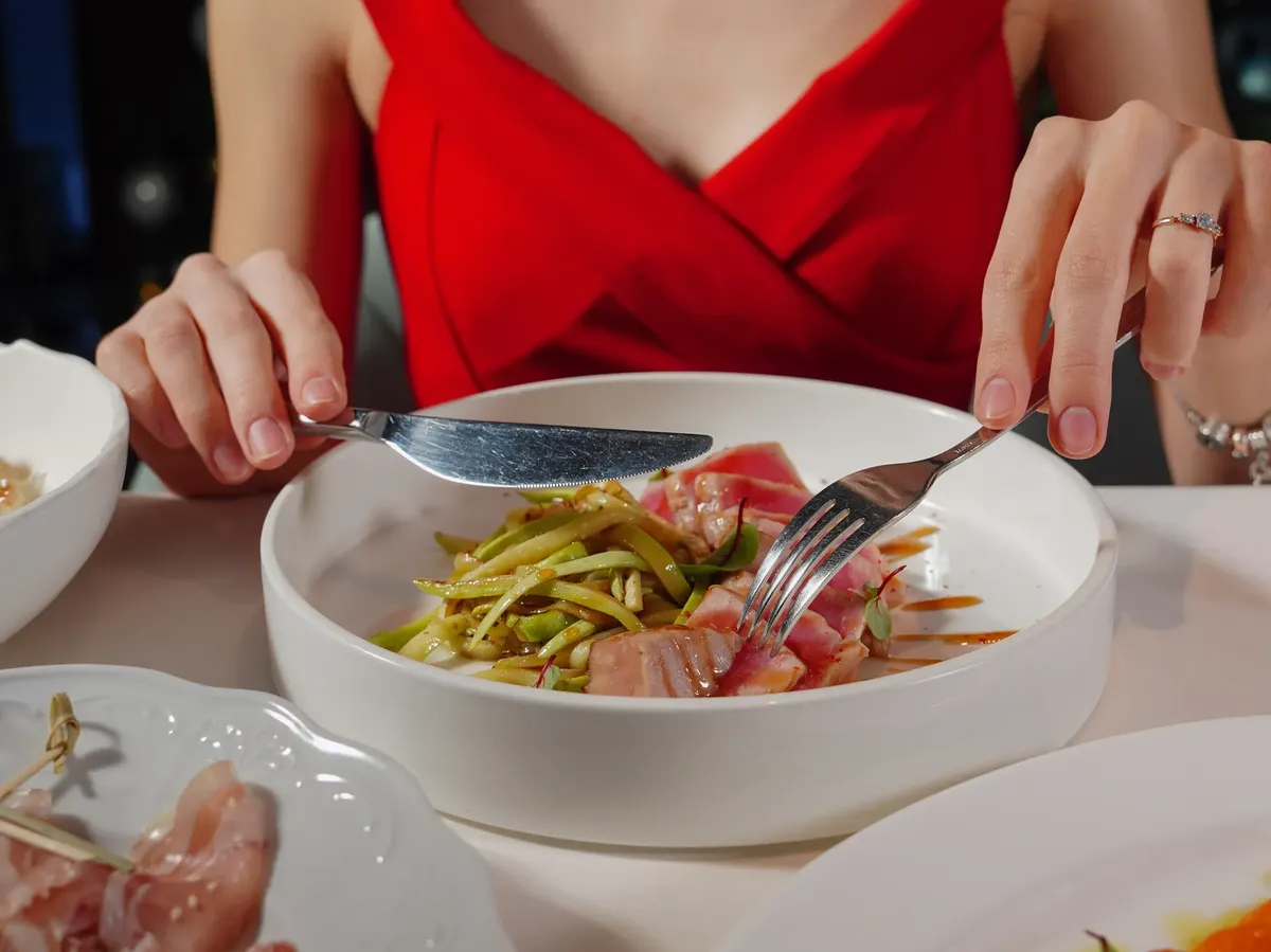 Woman in red dress enjoying a gourmet tuna and asparagus meal. Perfect for culinary and lifestyle themes.