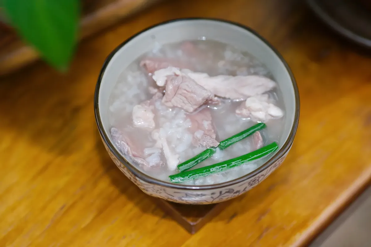 A warm bowl of homemade Asian pork and rice soup with green garnishes, perfect for comfort food lovers.