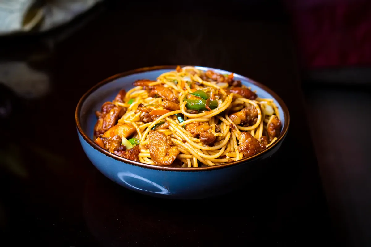 Freshly cooked chicken chow mein with vegetables in a blue bowl, ideal for food photography.