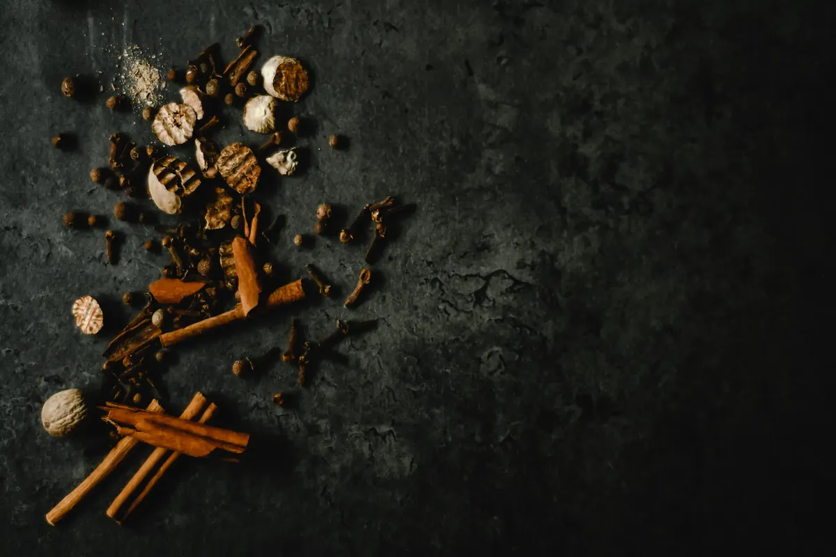 A mix of spices including cinnamon and cloves on a textured dark countertop.