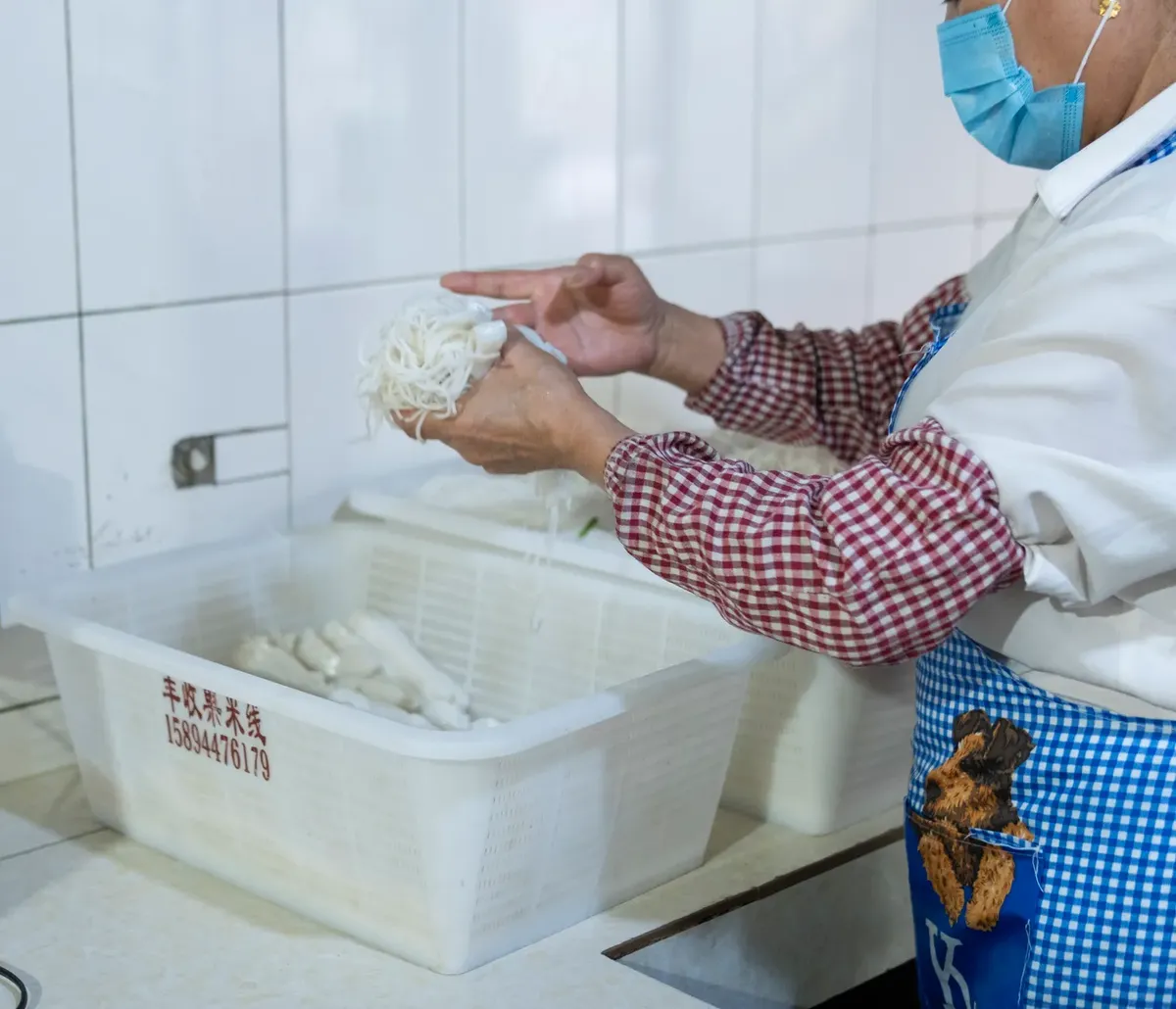 Person preparing rice noodles in a traditional Yunnan kitchen setting.