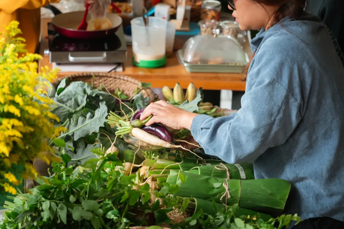 Woman choosing vegetables at a vibrant market stall, filled with fresh greens and herbs.